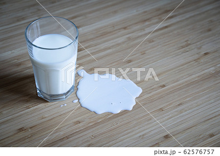 glass on wooden table with milk spilled over in a 62576757