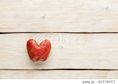 Ugly potato in the heart shape on a white wooden 62578457