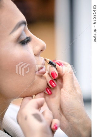 Fragment of girl face and hand of makeup artist painting lips Fragment of girl face and hand of makeup artist painting lips 62581485