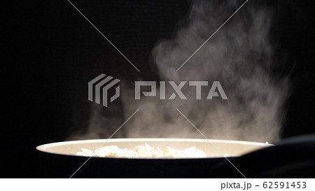 Frying pan with white thick steam in restaurant kitchen on a black background. Cooking chicken meat Frying pan with white thick steam in restaurant kitchen on a black background. Cooking chicken meat 62591453