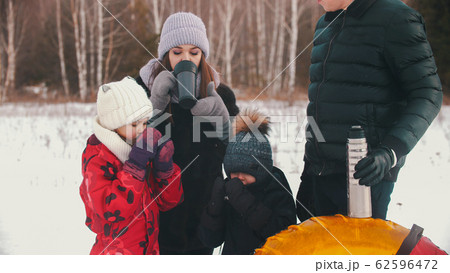 Mother and father with two little kids standing outdoors drinking hot drinks from the thermos Mother and father with two little kids standing outdoors drinking hot drinks from the thermos 62596472