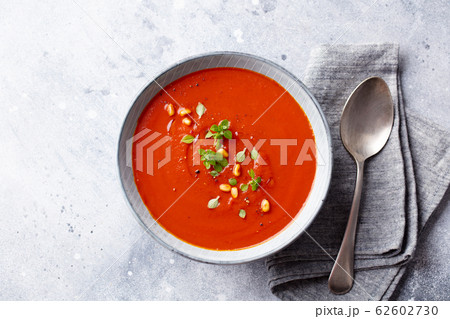 Tomato soup with fresh herbs and pine nuts in a bowl. Grey stone background. Top view. 62602730