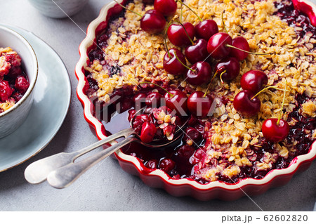 Cherry, red berry crumble in baking dish. Grey stone background. Close up. Cherry, red berry crumble in baking dish. Grey stone background. Close up. 62602820