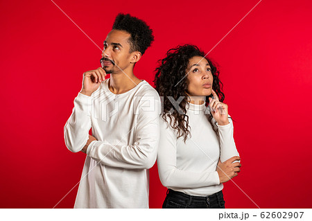 Portrait of young thinking pondering couple on red studio background. Man and woman look in different directions and everyone thinks about his problem. 62602907