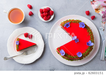 Raspberry layerd cake decorated with violet flowers and tea cup. Grey stone background. Top view. 62603151