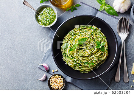 Pasta spaghetti with pesto sauce and fresh basil leaves in black bowl. Grey background. Copy space. Top view. 62603204