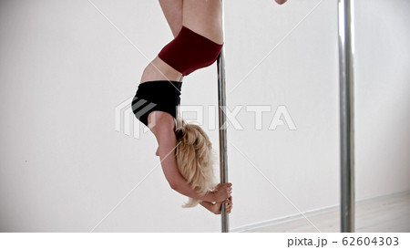 A blonde woman having a pole dancing training in the studio - keeping the balance upside down A blonde woman having a pole dancing training in the studio - keeping the balance upside down 62604303