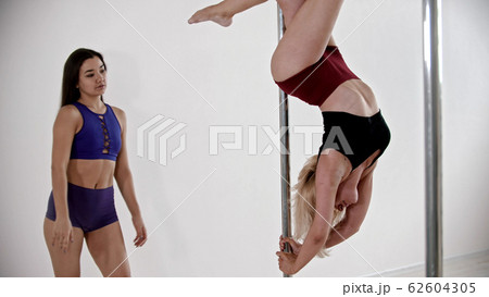 A blonde woman having a pole dancing training in the studio - keeping the balance upside down - her trainer watching her A blonde woman having a pole dancing training in the studio - keeping the balance upside down - her trainer watching her 62604305
