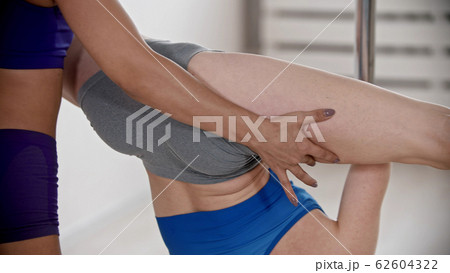 Two young women training pole dancing - trainer holding another woman's thighs upside down 62604322