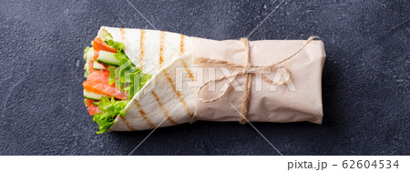 Wrap sandwich, roll with fish salmon and vegetables. Dark background. Top view. 62604534