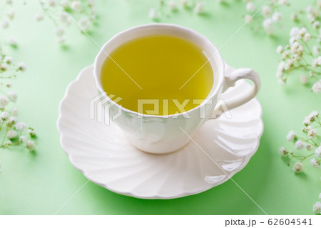 Green tea in a white cup with gypsophila flowers on green pastel background. Close up. Green tea in a white cup with gypsophila flowers on green pastel background. Close up. 62604541
