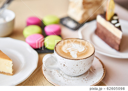 Breakfast in the cafe, morning coffee. Cappuccino and lots of desserts on the table. Napoleon, chocolate cake, cheesecake and macaroons. Breakfast in the cafe, morning coffee. Cappuccino and lots of desserts on the table. Napoleon, chocolate cake, cheesecake and macaroons. 62605098