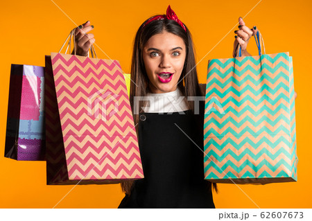 Happy young woman with long hair with paper bags after shopping isolated on yellow studio background. Seasonal sale, purchases, spending money on gifts concept 62607673