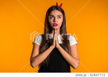 Cute young girl with beautiful hairstyle praying over yellow background. Woman begging someone. Cute young girl with beautiful hairstyle praying over yellow background. Woman begging someone. 62607715