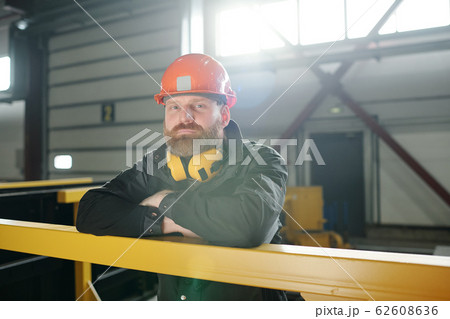Young bearded man in protective workwear standing by yellow bar Young bearded man in protective workwear standing by yellow bar 62608636