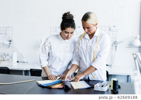 Two young female fashion designers consulting about choice of fabric 62609188