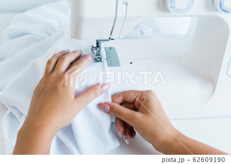 Hands of young female with white textile sitting by electric machine and sewing 62609190