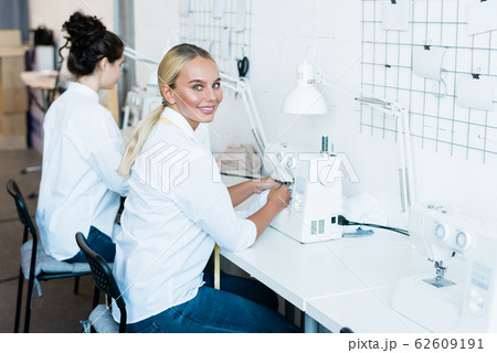Young cheerful seamstress in jeans and white shirt looking at you during work 62609191