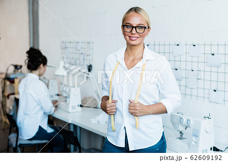 Happy young blonde seamstress with measuring tape looking at you 62609192