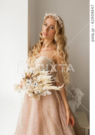 Young bride in a beautiful dress and wreath on her head holding a bouquet of flowers in bright white studio. Wedding concept. Young bride in a beautiful dress and wreath on her head holding a bouquet of flowers in bright white studio. Wedding concept. 62609647