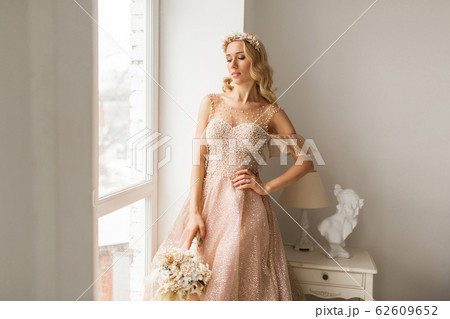 Young bride in a beautiful dress and wreath on her head holding a bouquet of flowers in bright white studio. Wedding concept. 62609652