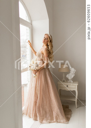 Young bride in a beautiful dress and wreath on her head holding a bouquet of flowers in bright white studio. Wedding concept. 62609653