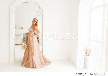 Young bride in a beautiful dress and wreath on her head holding a bouquet of flowers in bright white studio. Wedding concept. Young bride in a beautiful dress and wreath on her head holding a bouquet of flowers in bright white studio. Wedding concept. 62609663