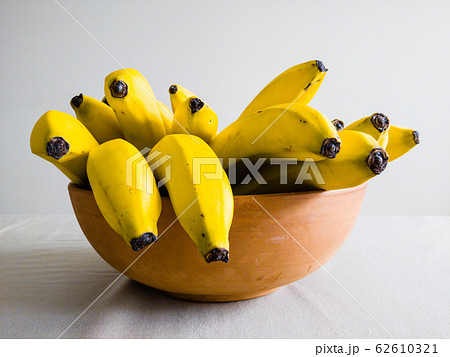 Many bananas in bowl on table viewed from side. 62610321