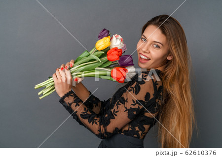 Young woman in black dress studio isolated on gray holding tulips bouquet 62610376