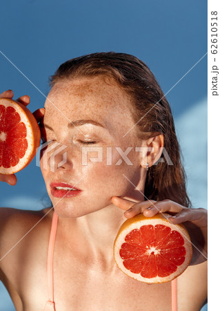 Summer Freestyle. Young woman with freckles and wet hair standing isolated on blue posing with grapefruit halves closed eyes delightful top view Summer Freestyle. Young woman with freckles and wet hair standing isolated on blue posing with grapefruit halves closed eyes delightful top view 62610518
