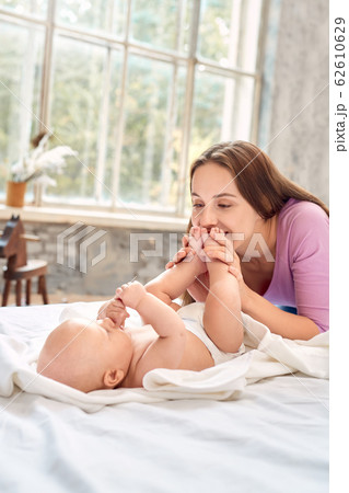 Young adult mom kissing feet her little newborn baby 62610629