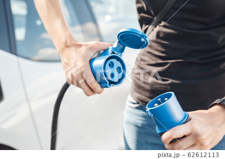 Transportation. Young man traveling by electric car stop at chraging station power in battery via EV charging socket and plug close-up Transportation. Young man traveling by electric car stop at chraging station power in battery via EV charging socket and plug close-up 62612113