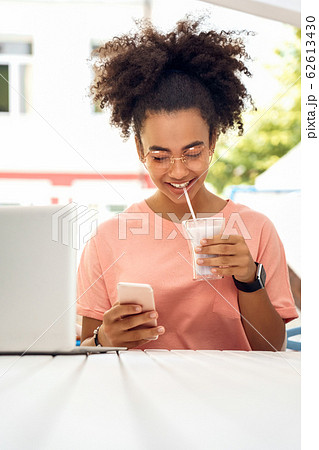 In the Cafe. Young girl in glasses sitting at table drinking milkshake using social media on smartphone cheerful 62613430