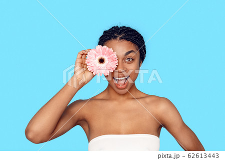 Beauty Concept. Young african woman isolated on blue covering eye with flower smiling excited 62613443