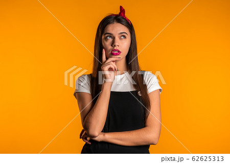 Thinking woman looking up on yellow background. Worried contemplative face expressions. Pretty girl model with cute appearance. 62625313
