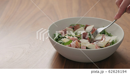 man hand pick salad with arugula, prosciutto and cherry tomatoes in white bowl on walnut table man hand pick salad with arugula, prosciutto and cherry tomatoes in white bowl on walnut table 62626194