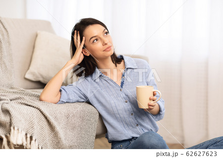 Cheerful young girl sitting on floor with cup of tea Cheerful young girl sitting on floor with cup of tea 62627623