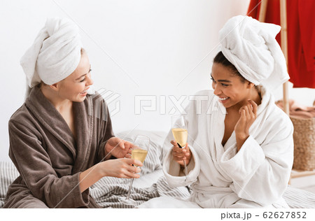 Multiracial girlfriends in bathrobes celebrating weekend, drinking champagne 62627852