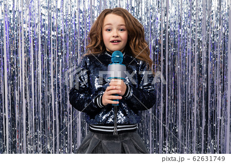 funny cheerful stylish girl with a microphone in her hands on a shiny tinsel background 62631749