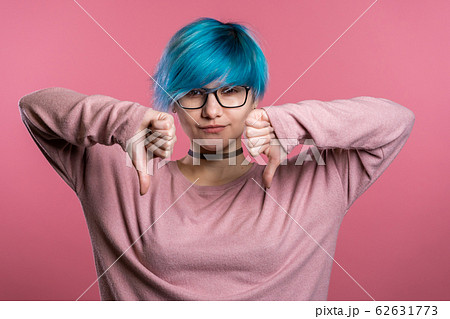 Young pretty woman with blue hair standing on pink studio background expressing discontent and showing thumb down gesture at camera. Portrait of girl with sign of dislike Young pretty woman with blue hair standing on pink studio background expressing discontent and showing thumb down gesture at camera. Portrait of girl with sign of dislike 62631773