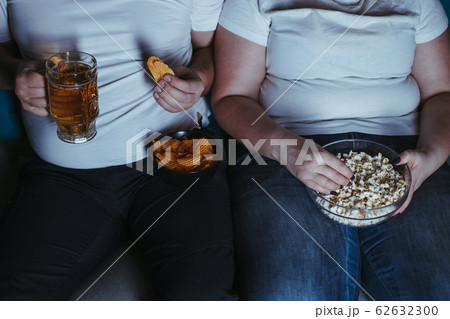 Overweight couple watching tv eating junk food 62632300
