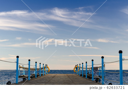 wooden platform with blue posts with ropes and orange lifebuoys on the background of the sea and sky with clouds wooden platform with blue posts with ropes and orange lifebuoys on the background of the sea and sky with clouds 62633721