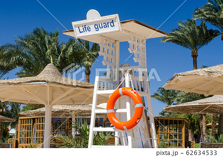 wooden lifeguard tower with orange lifebuoy on the beach against the backdrop of palm trees and reed parasols 62634533