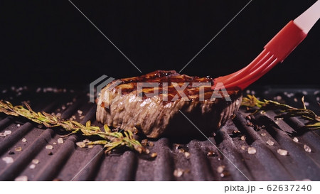 Delicious juicy meat steak cooking on grill. Prime rare roast grilling beef. Electric roaster, rosemary black pepper, salt. Silicone cooking brush. 62637240