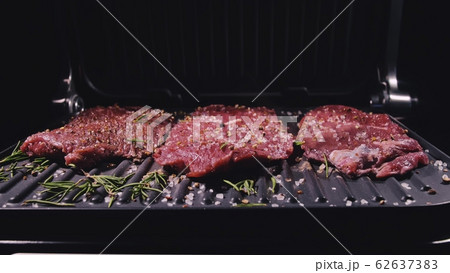 Delicious juicy meat steak cooking on grill. Prime beef fry on electric roaster, rosemary, black pepper, salt. Slow motion. 62637383