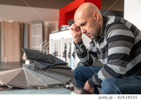 the man chooses the color of the new carpet according to the pattern book in the flooring shop the man chooses the color of the new carpet according to the pattern book in the flooring shop 62638505