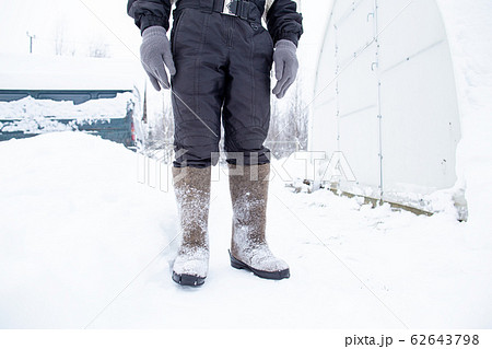 Man in warm felt boots and clothes stands on the trail, against the backdrop of a snowy courtyard. Man in warm felt boots and clothes stands on the trail, against the backdrop of a snowy courtyard. 62643798