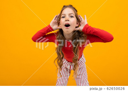 teenager girl with curly hair in a red blouse and striped trousers listens to the sounds on an 62650026