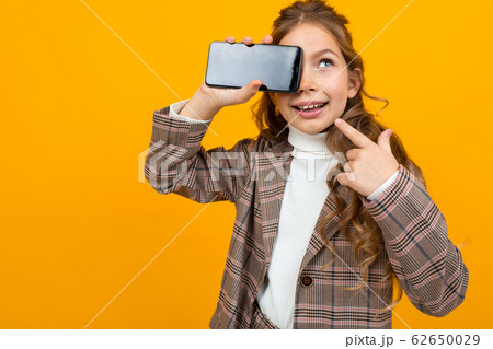 cute blonde girl in a classic jacket shows a phone with a mockup on a yellow background with copy cute blonde girl in a classic jacket shows a phone with a mockup on a yellow background with copy 62650029