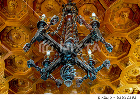 Beautiful carved wooden dark chandelier on a wooden patterned ceiling in an old manor Beautiful carved wooden dark chandelier on a wooden patterned ceiling in an old manor 62652392